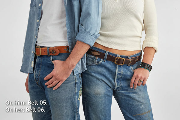 Two people in front of a white background wearing jeans and light shirts, both wearing brown leather studded belts
