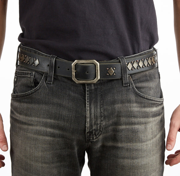 Person wearing dark jeans and a studded belt with a repeating diamond and circle stud design on a white background