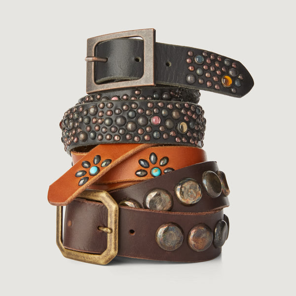 Three leather belts with a variety of decorative studding designs, stacked on top of each other on a white background