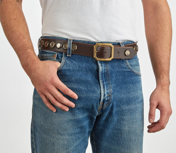 Man wearing a white shirt, blue jeans, and a brown leather belt with bottlecap studs